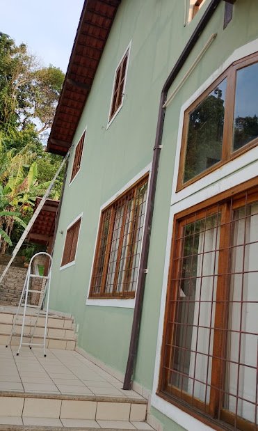 Fachada verde-sálvia com janelas de madeira envernizadas
